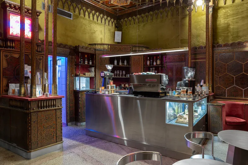 Stainless steel coffee counter beneath ornate timber wall panels and coffered ceiling with blue accent lighting