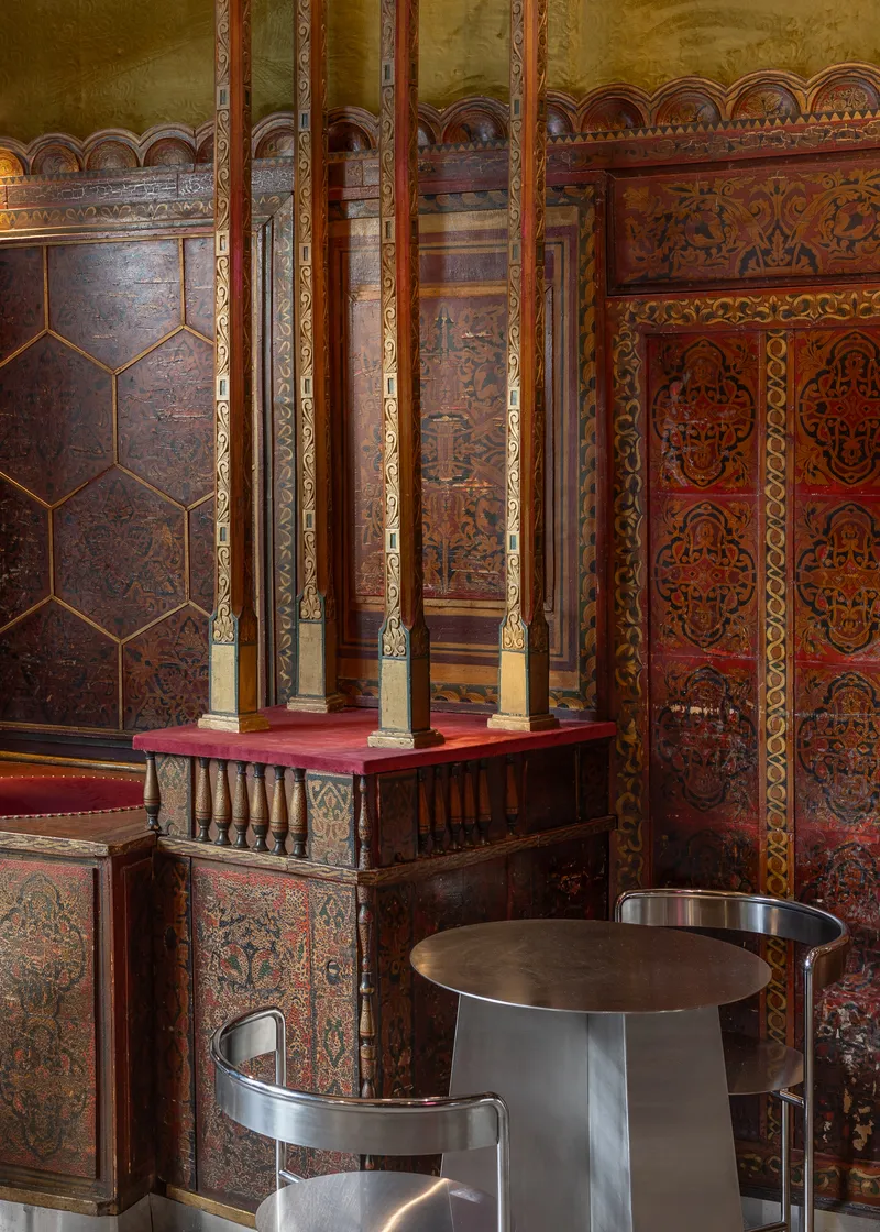 Slim brass columns supporting a red platform against walls clad in patterned timber panels and carved wainscoting