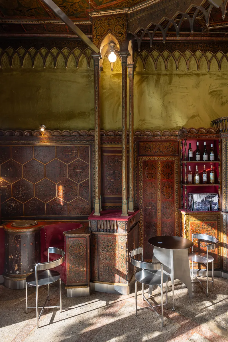Interior space with steel chairs on terrazzo flooring beneath pointed archways illuminated by wall sconces at dusk