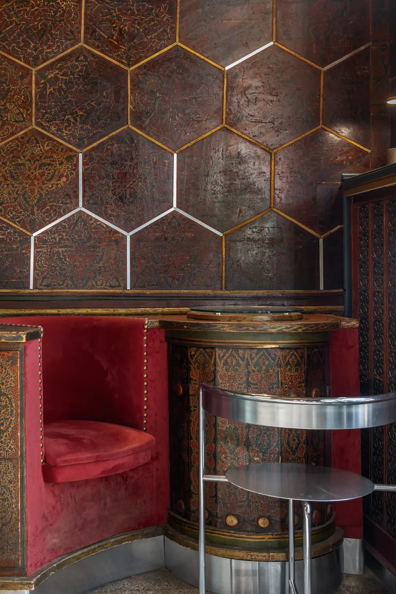 Hexagonal brass trim dividing embossed wall panels above a banquette and curved stainless steel table