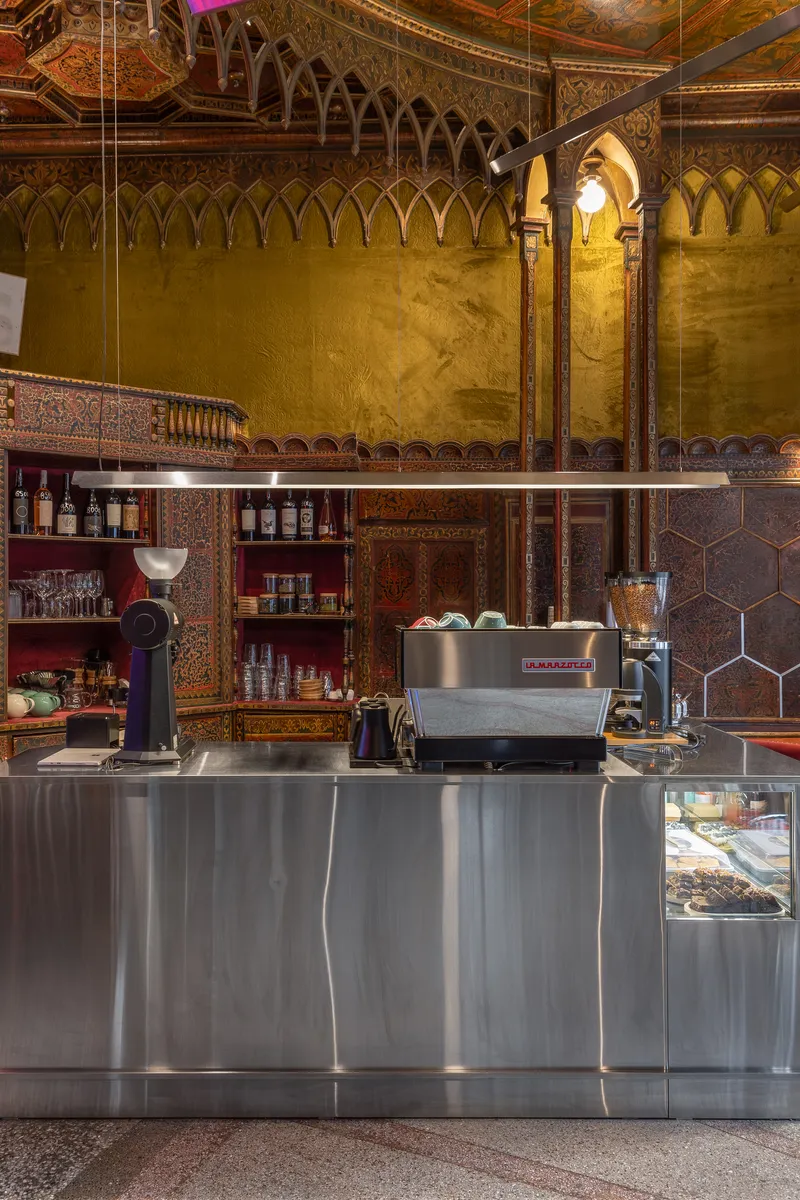 Stainless steel service counter with espresso machine beneath arched openings and a suspended glass display case