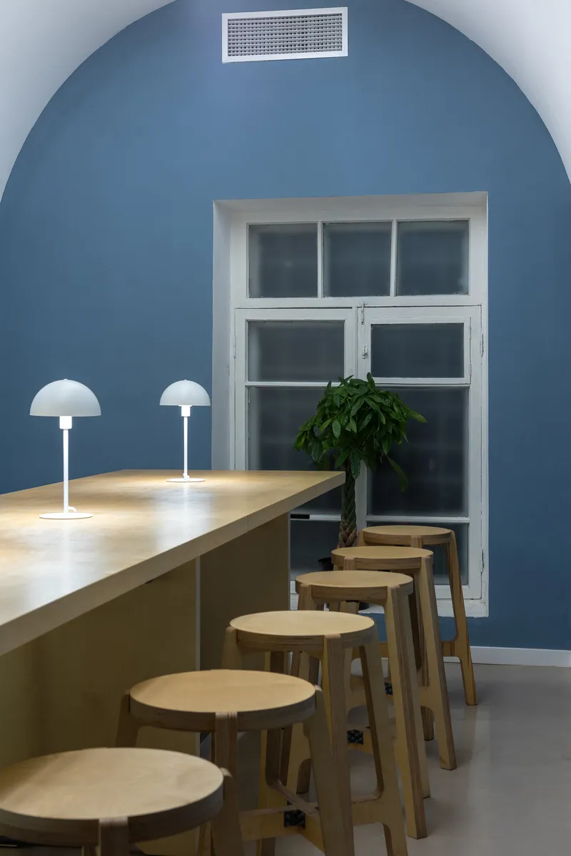 Arched blue wall with white-framed door behind a timber bar counter lined with wooden stools