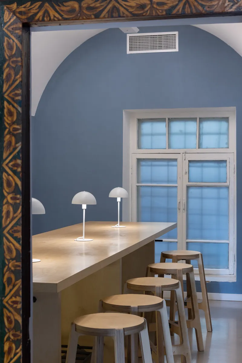 View through ornate doorframe to blue arched dining area with timber counter and mushroom lamps