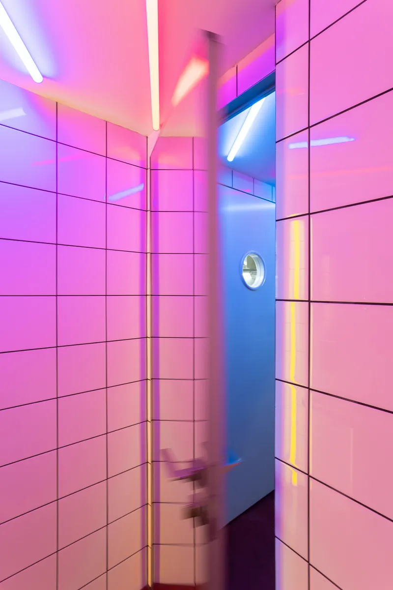 Tiled hallway with pink and blue neon lighting and motion-blurred figure passing through