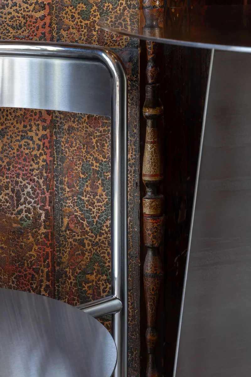 Detail of tubular steel chair back against a textured mural wall with exposed bamboo column