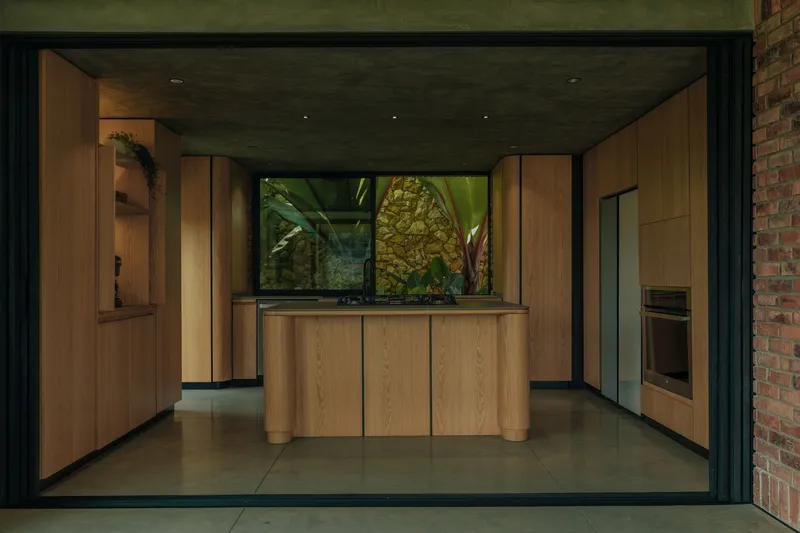 Kitchen with oak cabinetry and central island viewed through open sliding glass doors at dusk