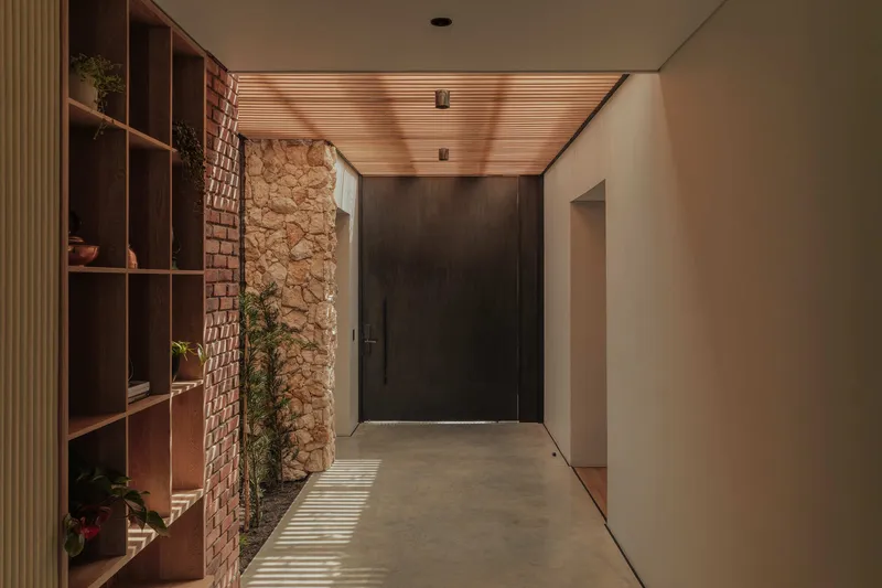 Interior hallway with timber slatted ceiling, brick wall, stone wall and wooden shelving catching afternoon light