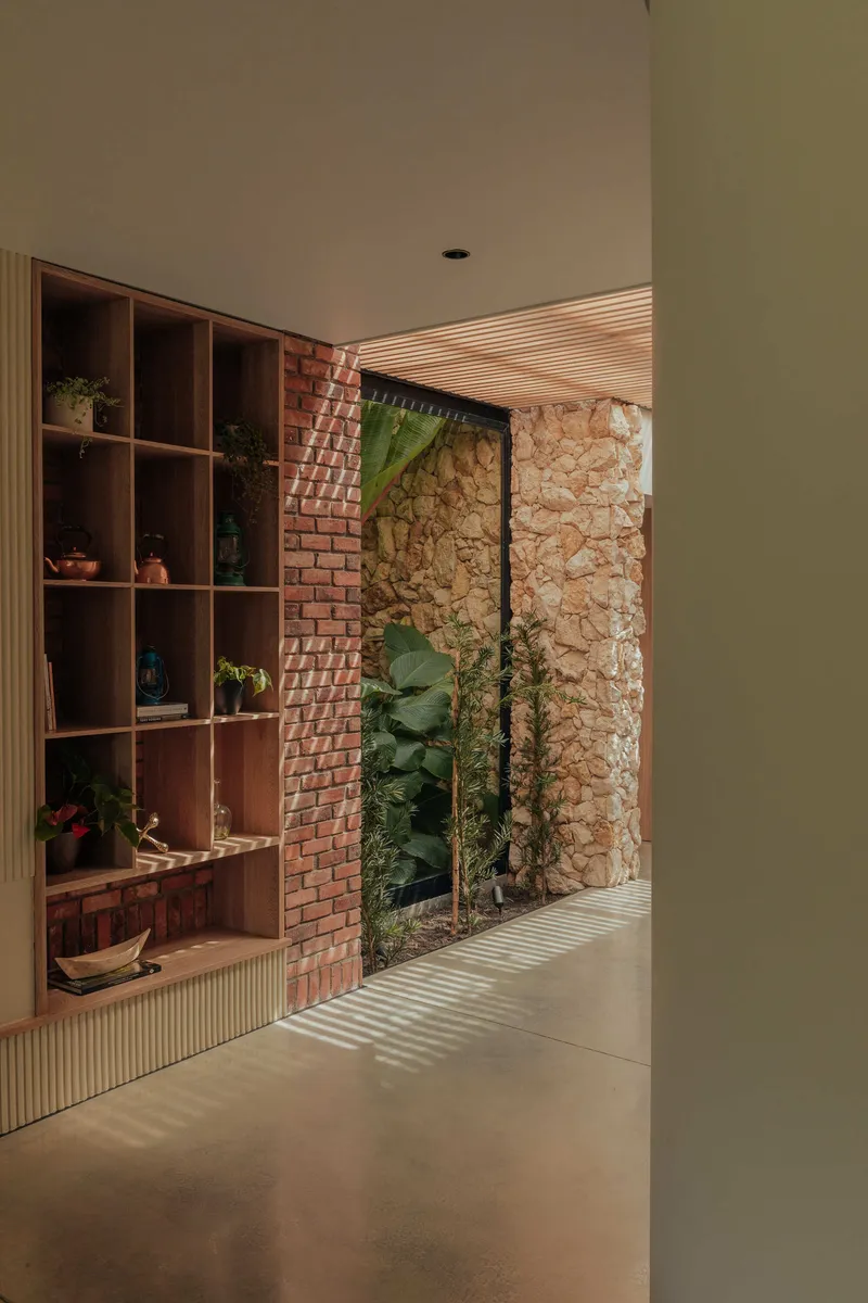 Interior hallway with timber shelving unit, red brick column and limestone wall framing courtyard view
