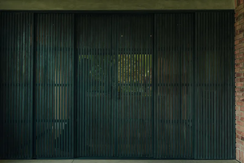 Dark timber vertical slat screen with glimpses of greenery visible through the gaps