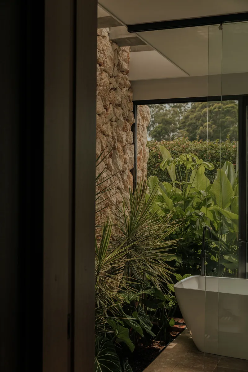 Interior corner with rough stone wall and planted bed beside a glass wall overlooking garden vegetation