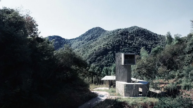 Concrete structure with tower and horizontal canopy set against forested mountain slopes