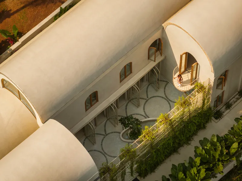 Aerial view of vaulted roof forms sheltering courtyard with circular pavers and planted balconies in afternoon light