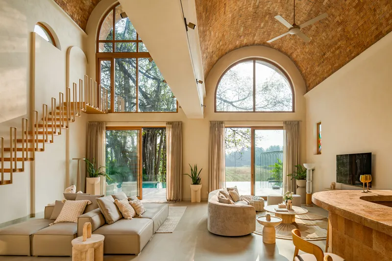 Double-height living room with vaulted brick ceiling, arched windows and suspended timber staircase in afternoon light