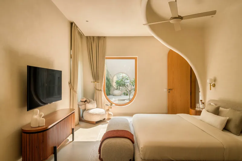 Bedroom with arched ceiling vault, circular window, and timber door framed by soft daylight
