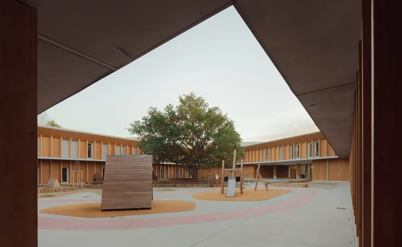 View through angled portal opening onto courtyard with central tree and timber-clad buildings