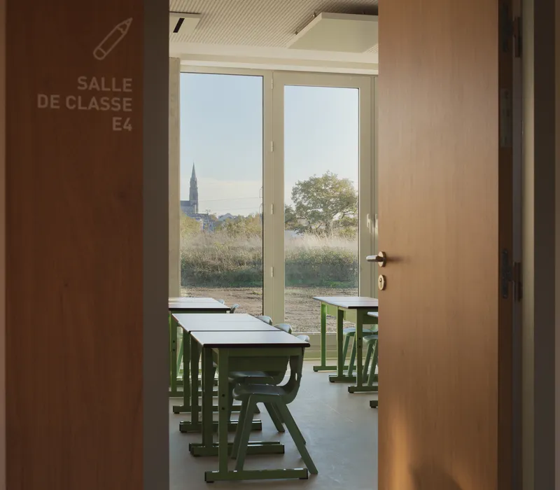 View through open door into classroom with green desks and church spire visible beyond window