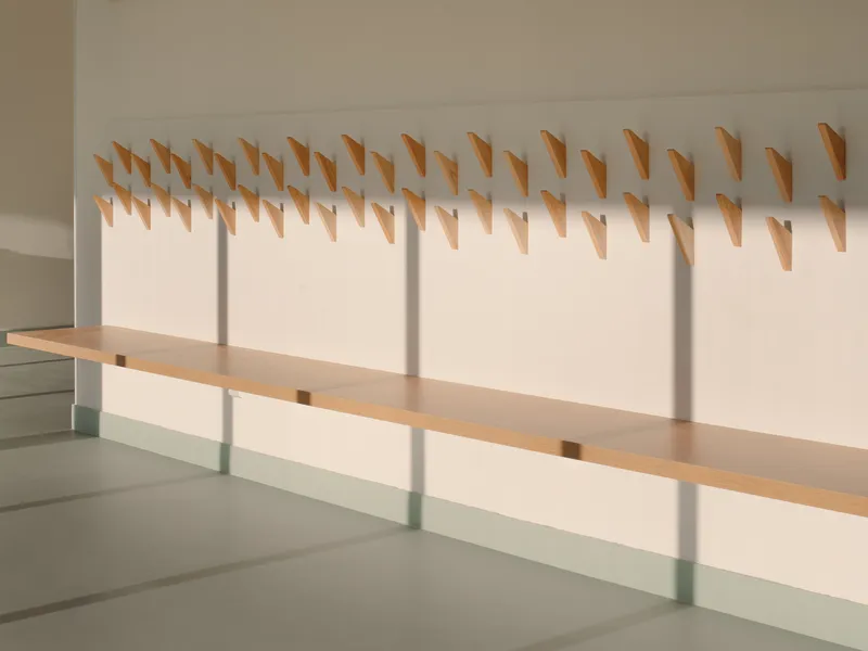 Wall-mounted timber coat hooks arranged in rows above pale green bench in afternoon light