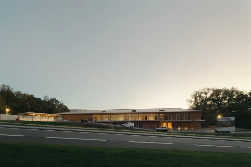 Long horizontal building with timber cladding and glazed sections viewed from across the road at twilight