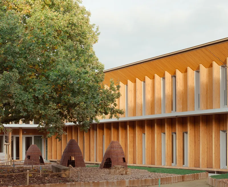 Courtyard with vertical timber cladding, woven pod structures and mature tree under overcast sky