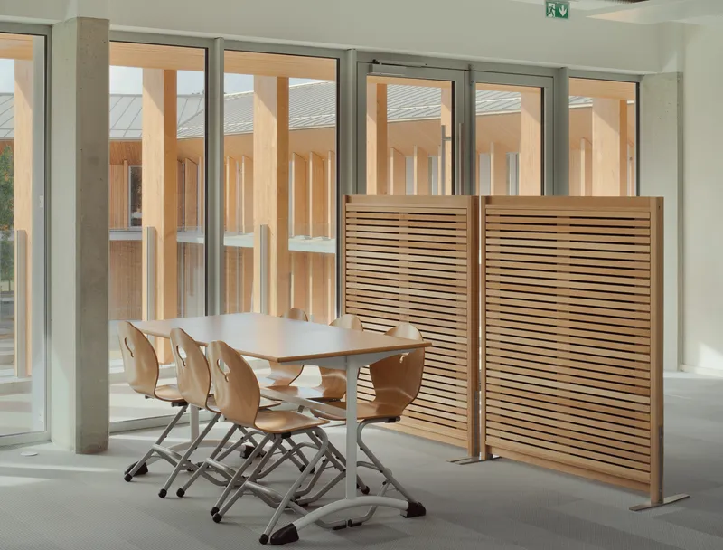 Meeting table with plywood chairs beside slatted timber screen and full-height glazing to courtyard