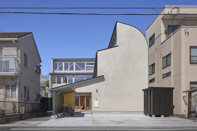 Street view of the curved white stucco facade nestled between neighboring houses under a clear blue sky