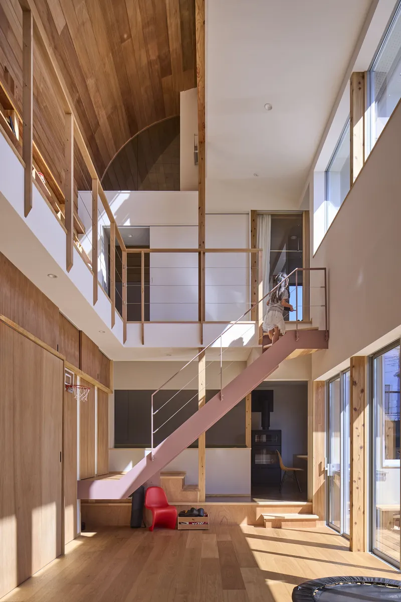View of the pink steel staircase connecting split-levels with timber paneling and sunlit openings