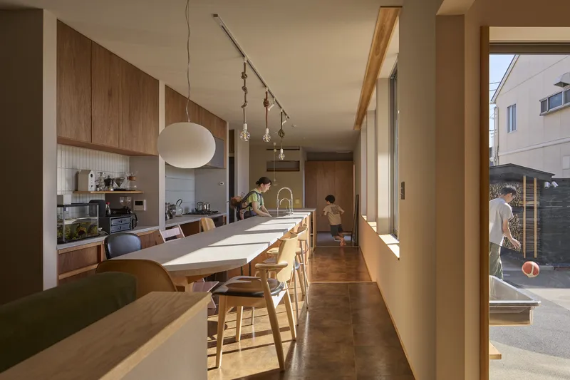 Kitchen and dining area with timber cabinetry and a long table flooded with afternoon sunlight