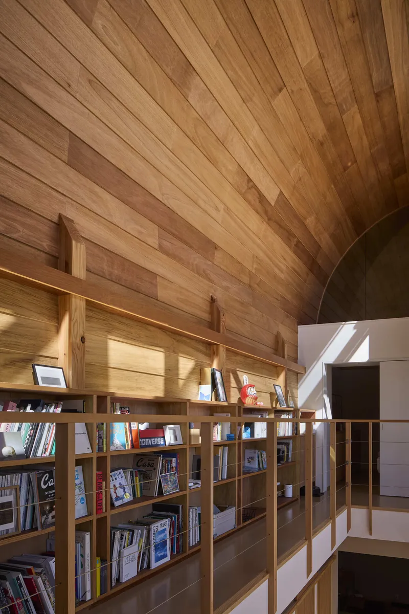 Curved wood plank ceiling above a bookshelf mezzanine with indirect lighting along the top shelves