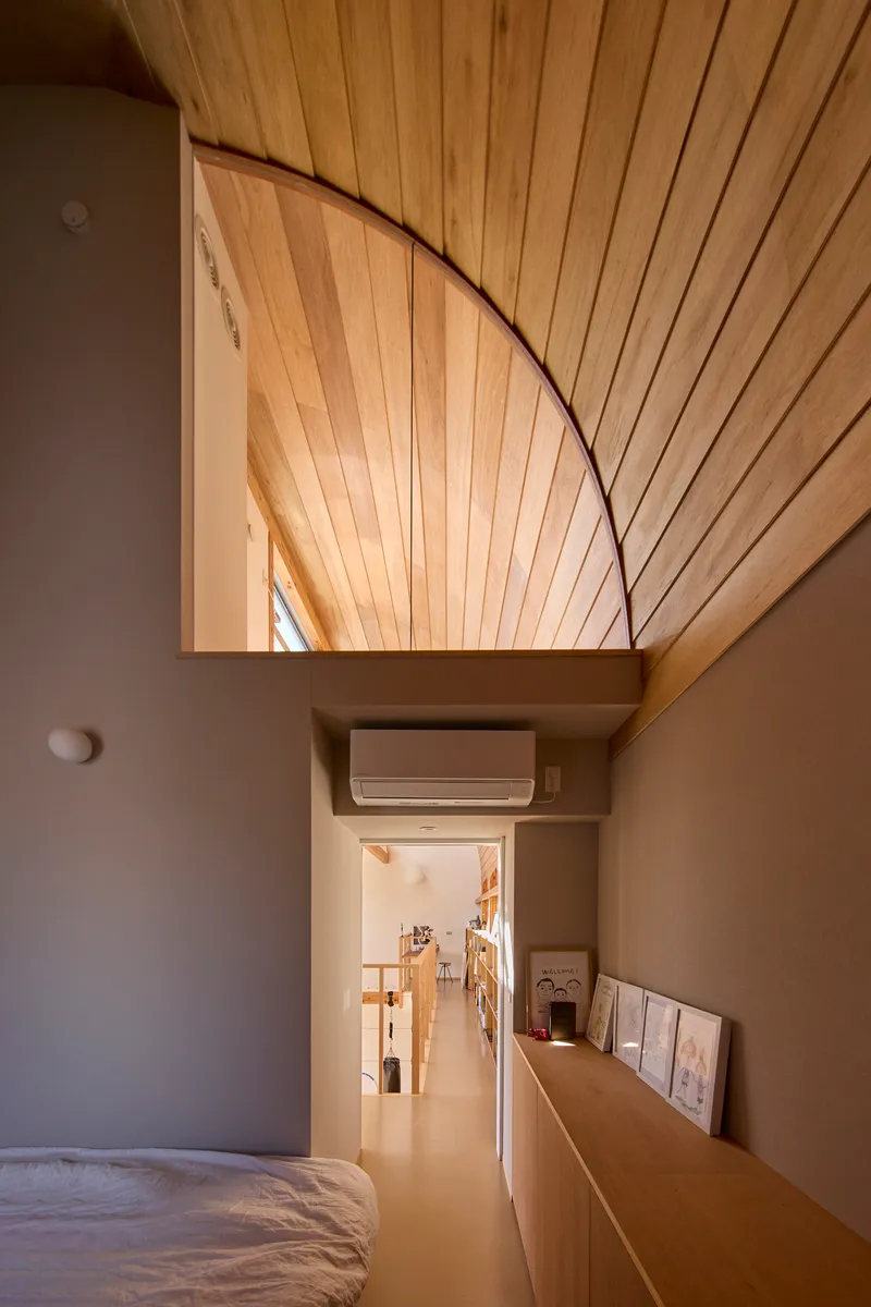 Bedroom view through a grey-framed opening showing the curved timber ceiling vault above a corridor