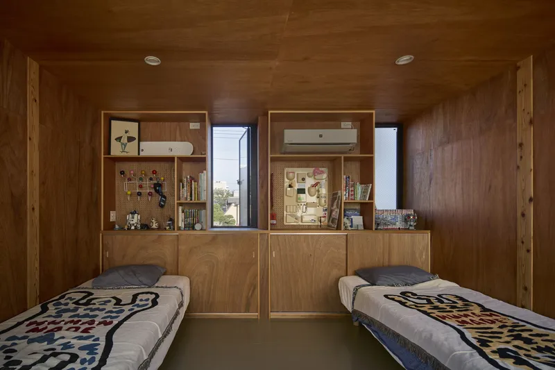 Twin beds in a wood-clad room with built-in storage and narrow windows framing views to neighboring rooftops