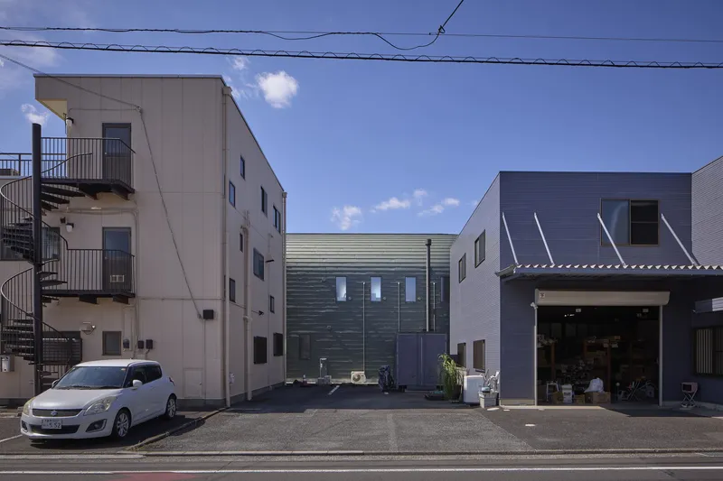 Street view of dark timber-clad facade flanked by neighboring buildings under a blue sky