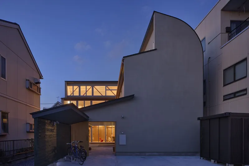 Illuminated glazed facade and curved roof volume visible from the courtyard at dusk