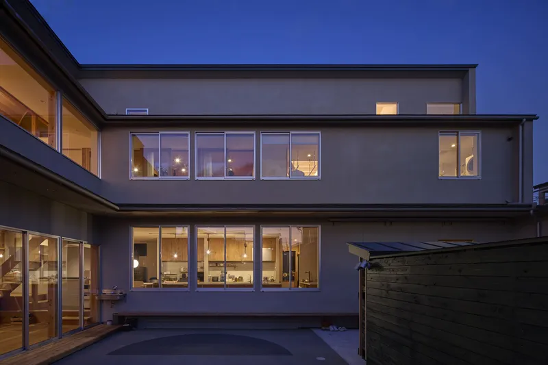 Two-story rear elevation with floor-to-ceiling windows lit from within at twilight