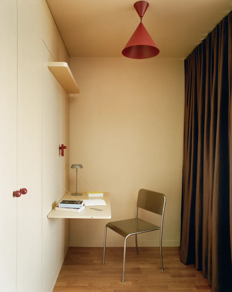 Built-in desk nook with folding wall-mounted surface and pendant light beside floor-length drapes