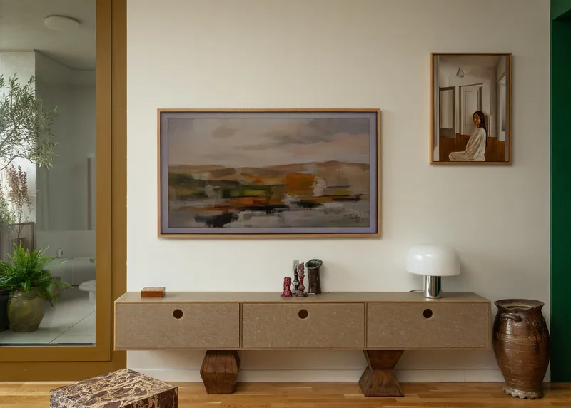 Low credenza with circular drawer pulls beneath framed artwork on a white wall near yellow-framed doorway