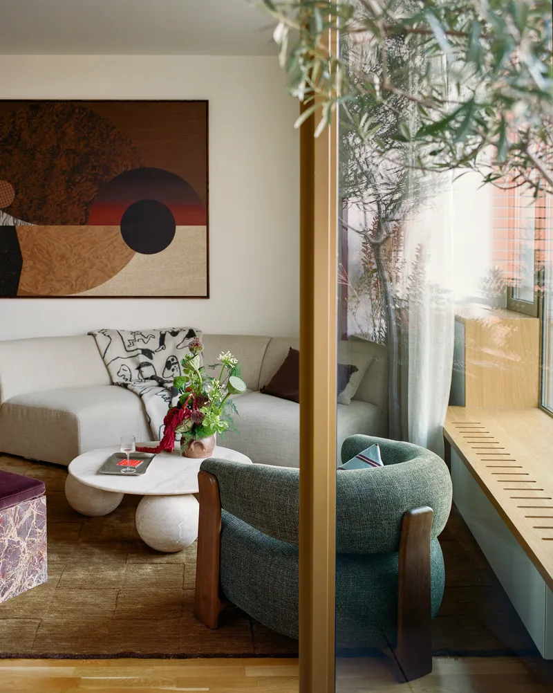 Brass-framed doorway separating interior seating from sunlit exterior terrace with olive tree