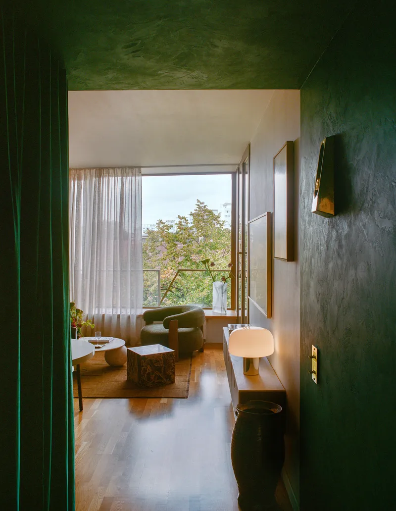 View through green plastered doorway toward a living room with tall windows overlooking tree canopy in daylight