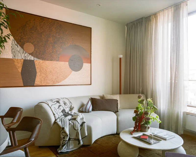 Living room corner with full-height sheer curtains at the window and painting above upholstered seating