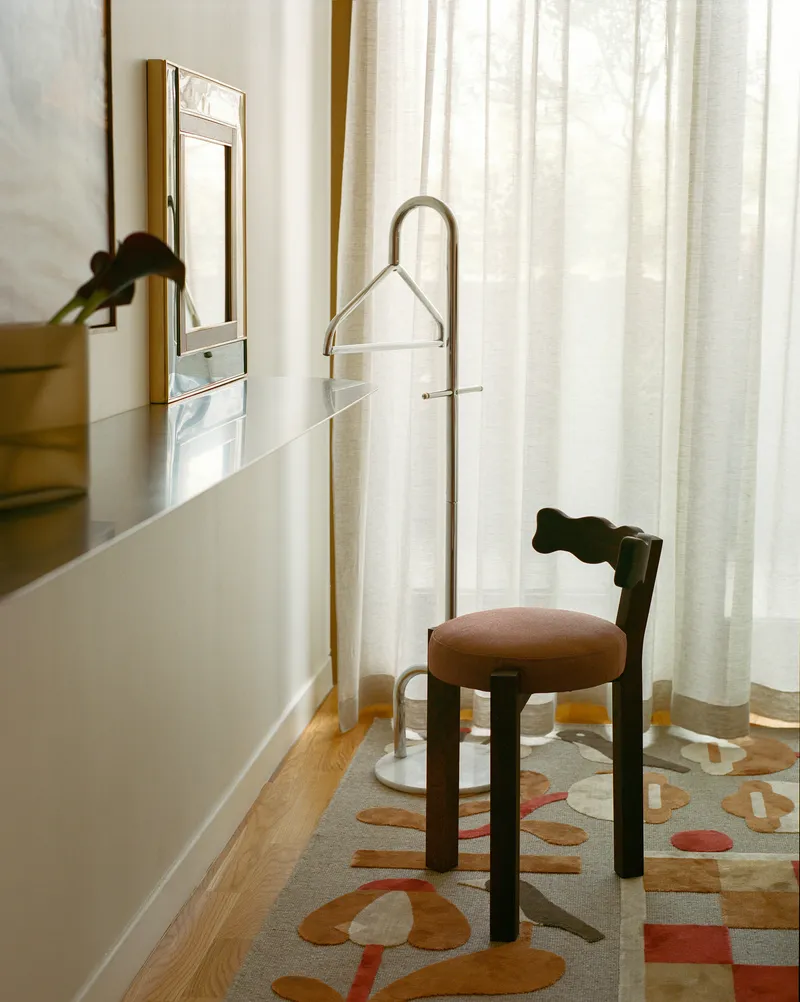 Metal clothes valet beside a patterned rug and sheer curtains in morning light
