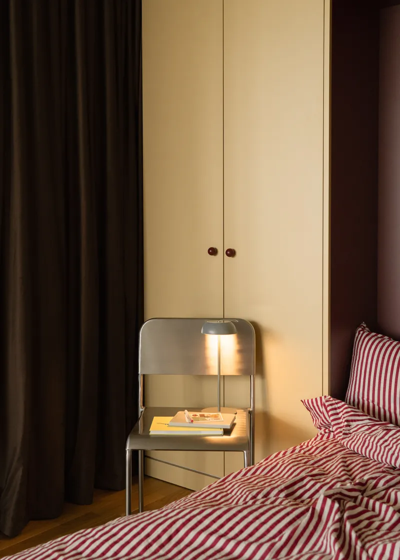 Pale yellow wardrobe with brown knobs beside a bedside table lamp in evening light