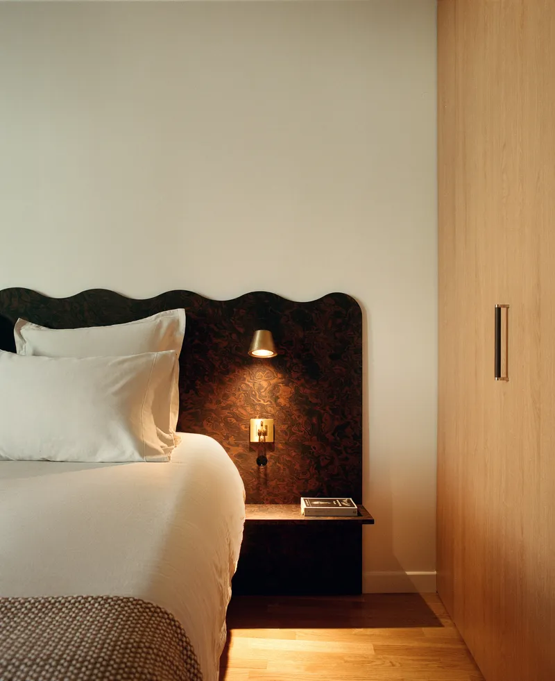 Dark burl wood headboard with integrated sconce lighting beside a floating nightstand