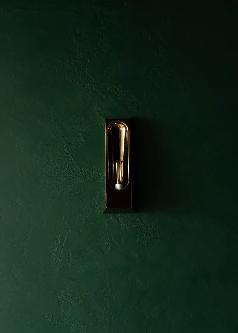 Black wall sconce with exposed filament bulb centered on a deep green plaster wall