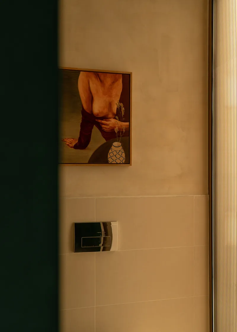 Bathroom wall detail with framed artwork above a flush plate and vertical timber cladding under warm light
