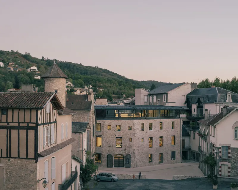 Stone building with illuminated windows nestled among historic village structures at dusk