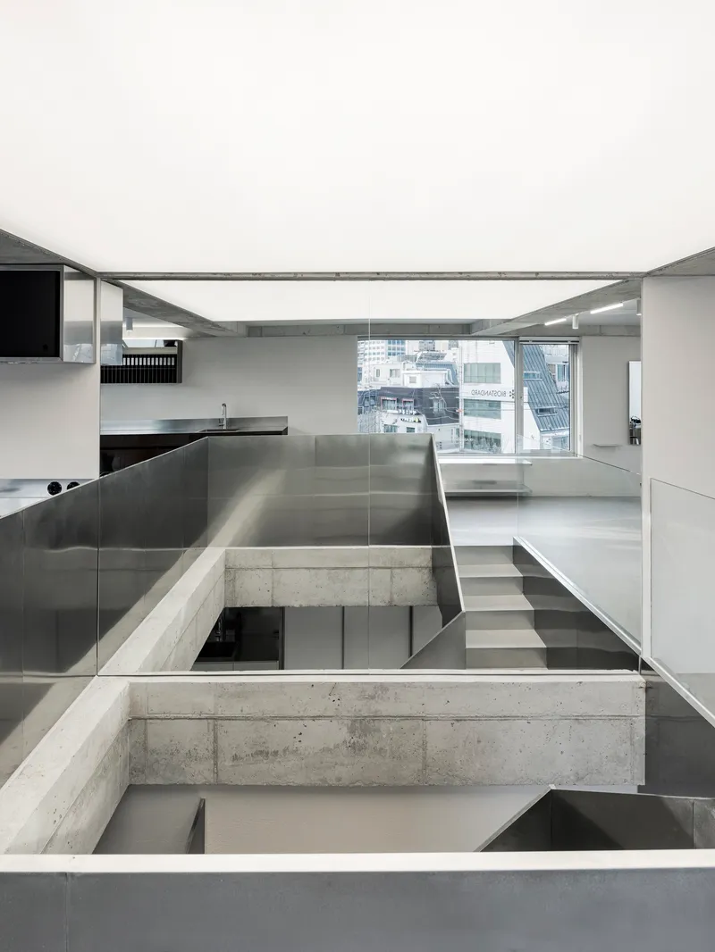 Split-level interior with stainless steel kitchen island and concrete beams crossing over glazed openings