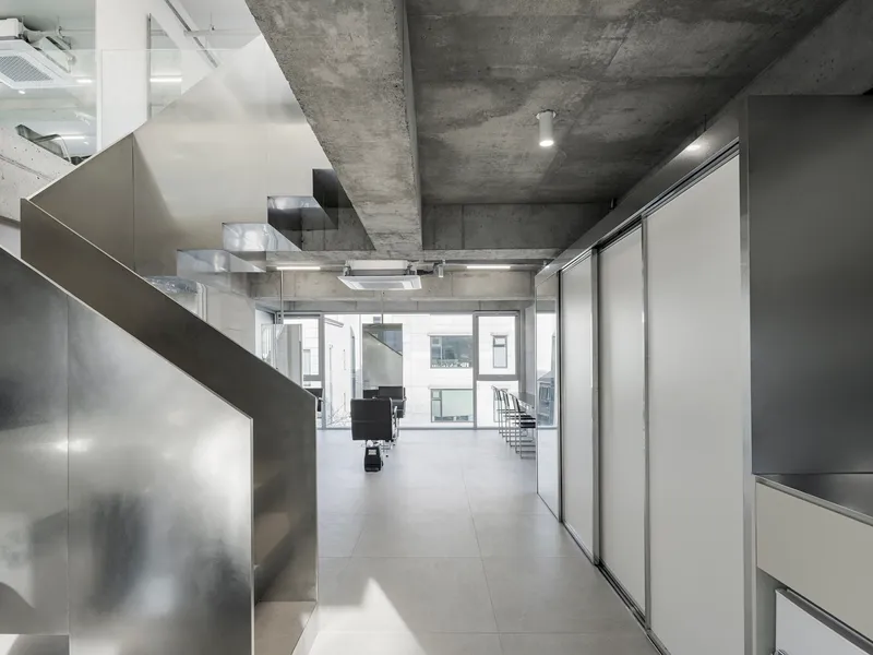 Corridor with exposed concrete ceiling beams, stainless steel partitions, and sliding white panels along the walls