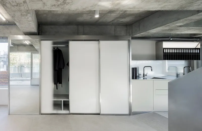Sliding white wardrobe doors partially open to reveal hanging garments, beside a kitchen with white countertops