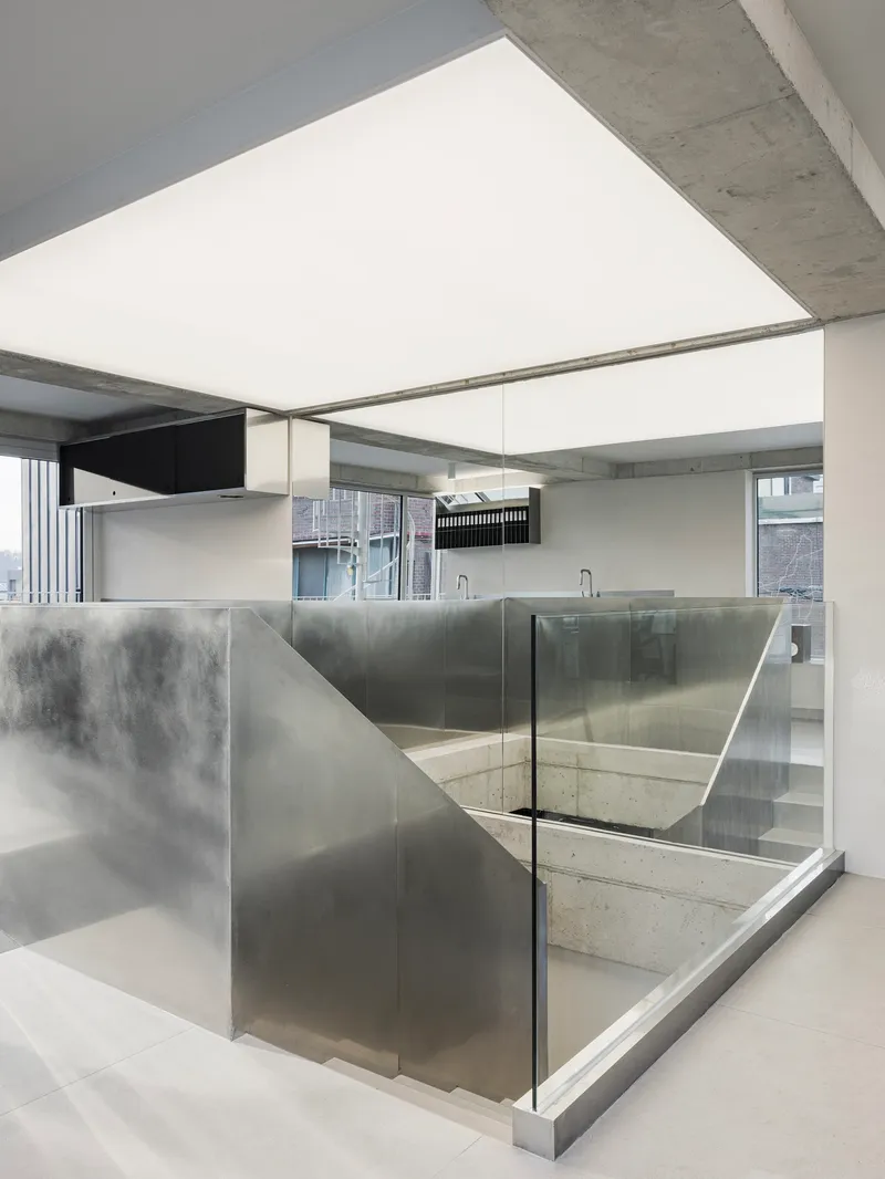 Concrete stairwell enclosed by translucent glass panels and brushed steel walls beneath an exposed ceiling