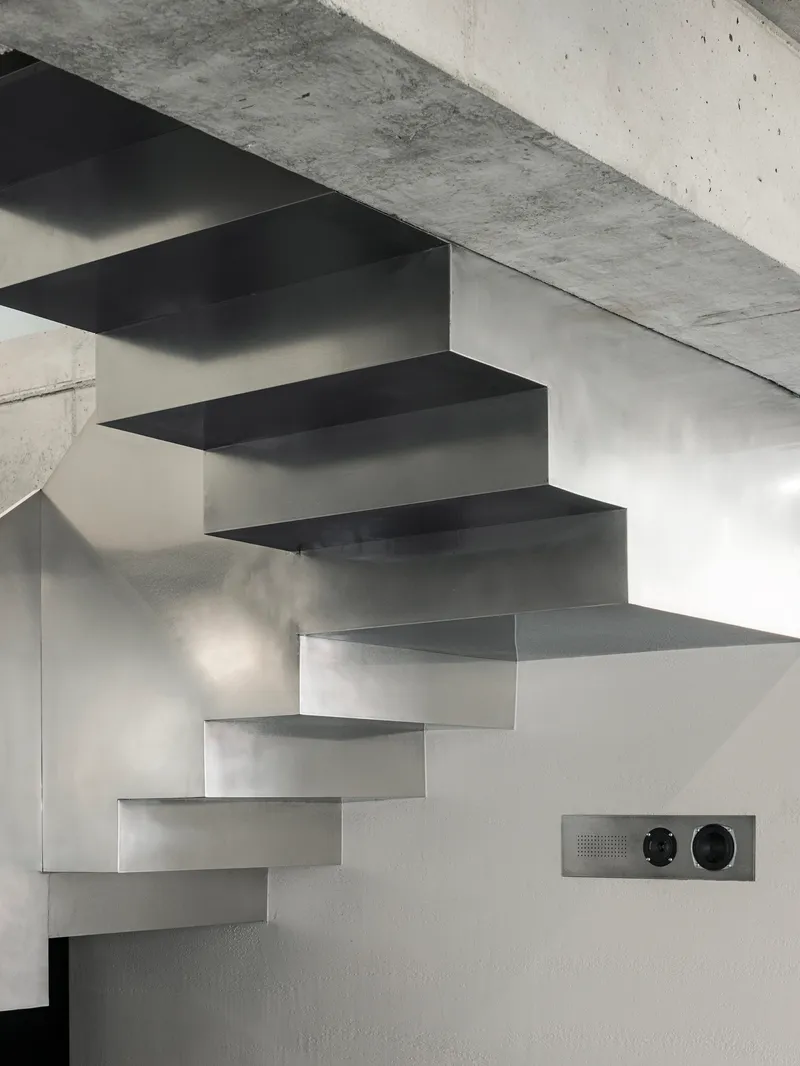 Cantilevered steel staircase with folded treads ascending against a white wall in natural light