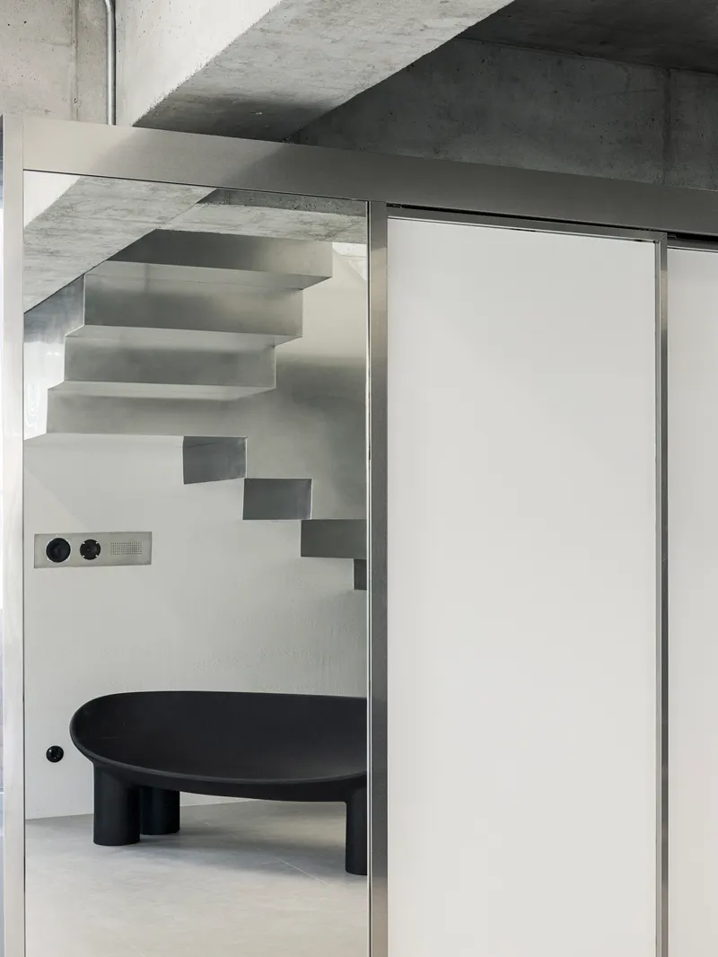 View through glass partition showing floating steel stairs and a black circular table below